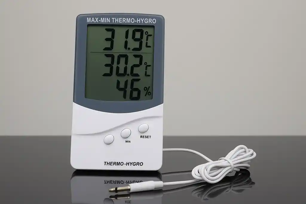 Medidor de temperatura y humedad relativa con sonda externa similar al termohigrómetro KTJ TA318 encima de una mesa de cristal negro y de fondo una pared blanca
