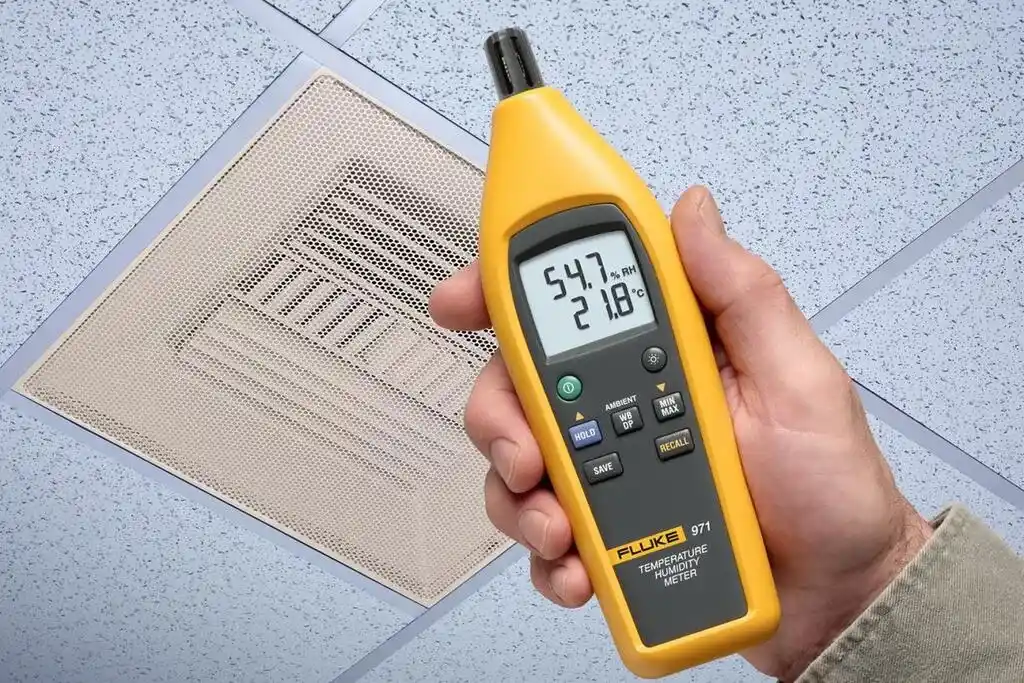 Termohigrómetro Fluke 971 sostenido por la mano de un técnico, midiendo la temperatura y humedad relativa ambiental del sistema HVAC de una oficina