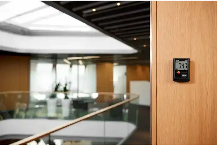 Mini termohigrómetro Testo 174H de color negro, fijado en la pared de madera en el interior de un elegante eldificio iluminado con luz natural que entra a través de sus ventanas y su gran lucernario