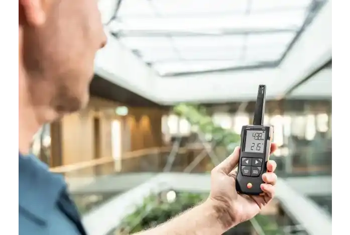 Técnico sosteniendo el termohigrómetro testo 625 mientras observa los valores de la pantalla, en el interior de un elegante edificio iluminado de forma natural a través de un gran lucernario