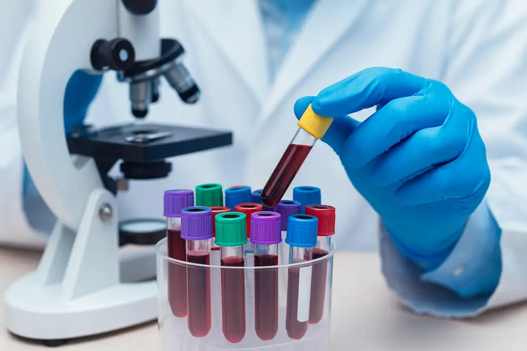 Científico con guantes azules manipulando tubos de ensayo con sangre junto a un microscopio